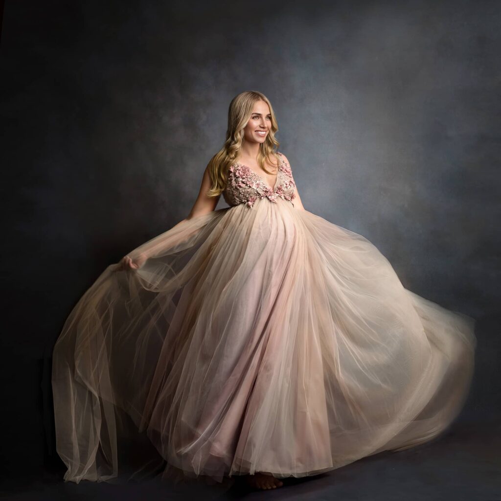 Schwangere junge blonde Frau im weitschwingenden roséfarbenen Tüll-Kleid beim Babybauch-Fotoshooting im Fotostudio Wuppertal