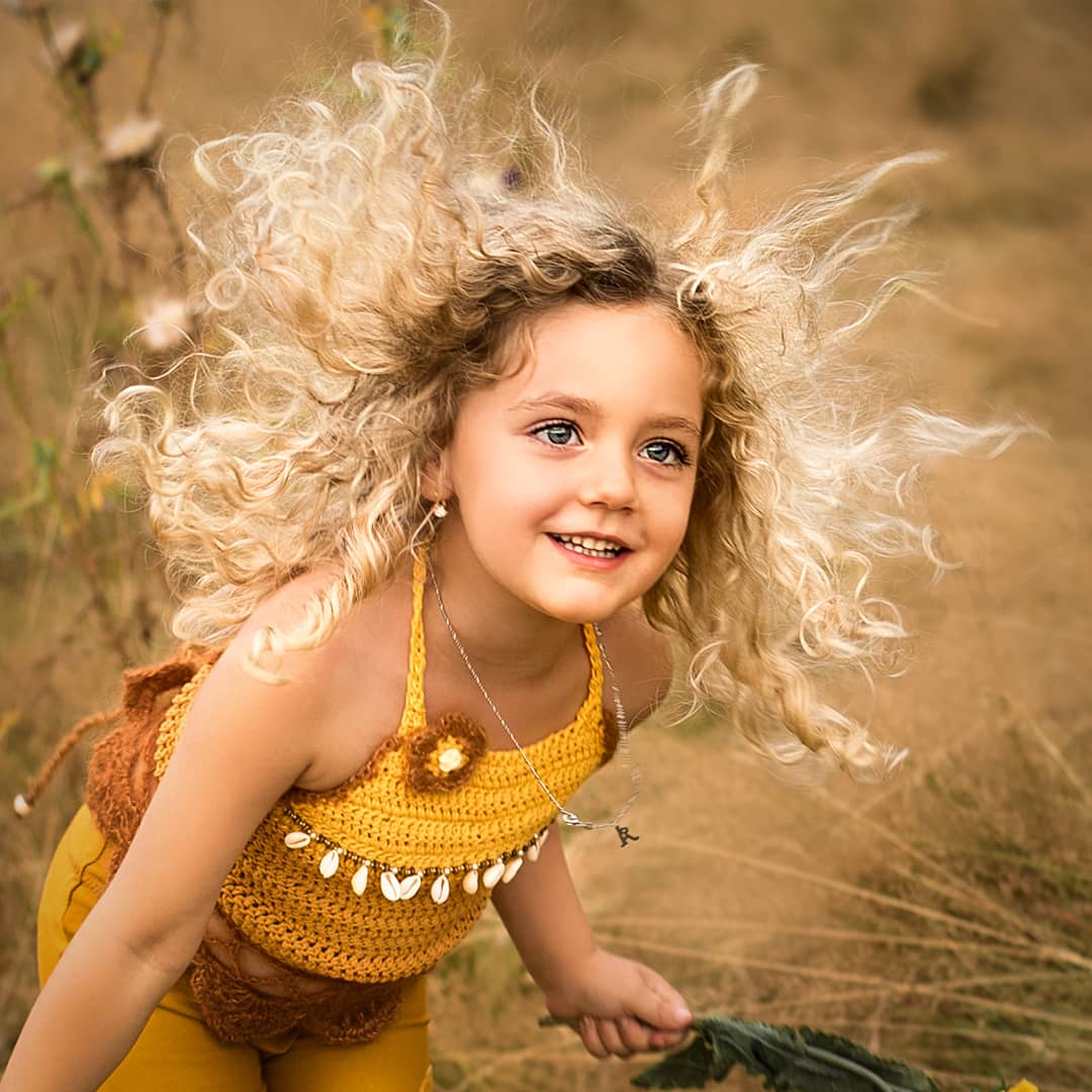 Authentisches Porträt eines lachenden Kindes mit wilden blonden Locken in einer sommerlichen Wiese beim ungestellten Kinder-Fotoshooting in Wuppertal