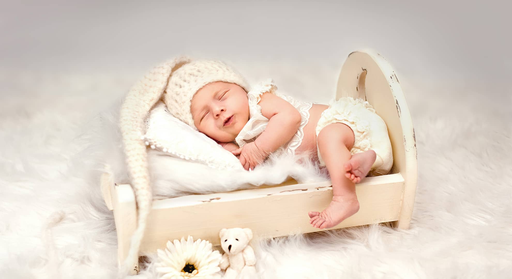 Baby mit zufriedenem Gesichtsausdruck und Zipfelmütze in Bett bei Neugeborenenfotos in Wuppertal