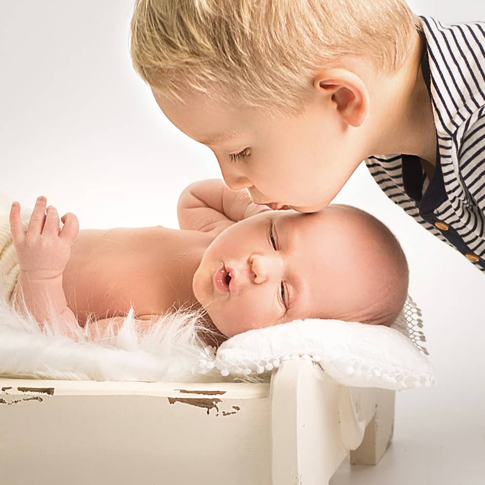 babyshooting-mit-bruder-in-wuppertal Ein kleiner Junge küsst seinen Baby Bruder sanft auf die Wange bei der Neugeborenenfotografin Josephine B. Scharrer
