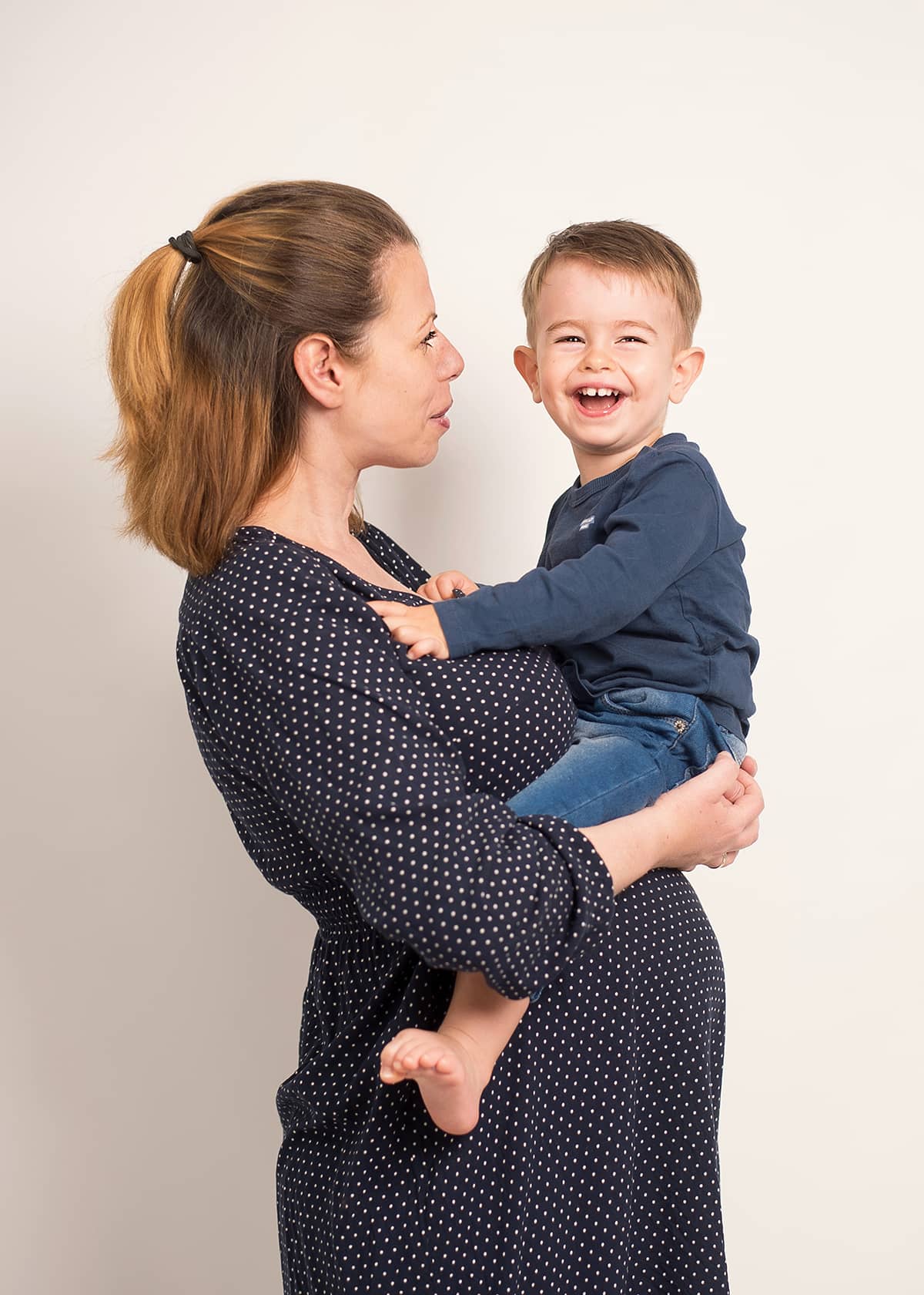 Werdende Mutter hält ihr lachendes Kleinkind auf dem Arm beim Babybauch-Fotoshooting als mobiles Homeshooting in Wuppertal.