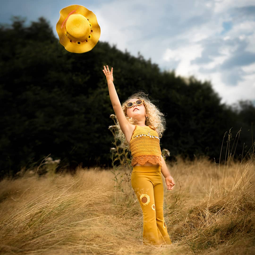 Ein kleines Kind wirft voller Freude seinen gelben Strohhut in den Himmel bei einem Wilde Herzen Kinder-Fotoshooting in Wuppertal