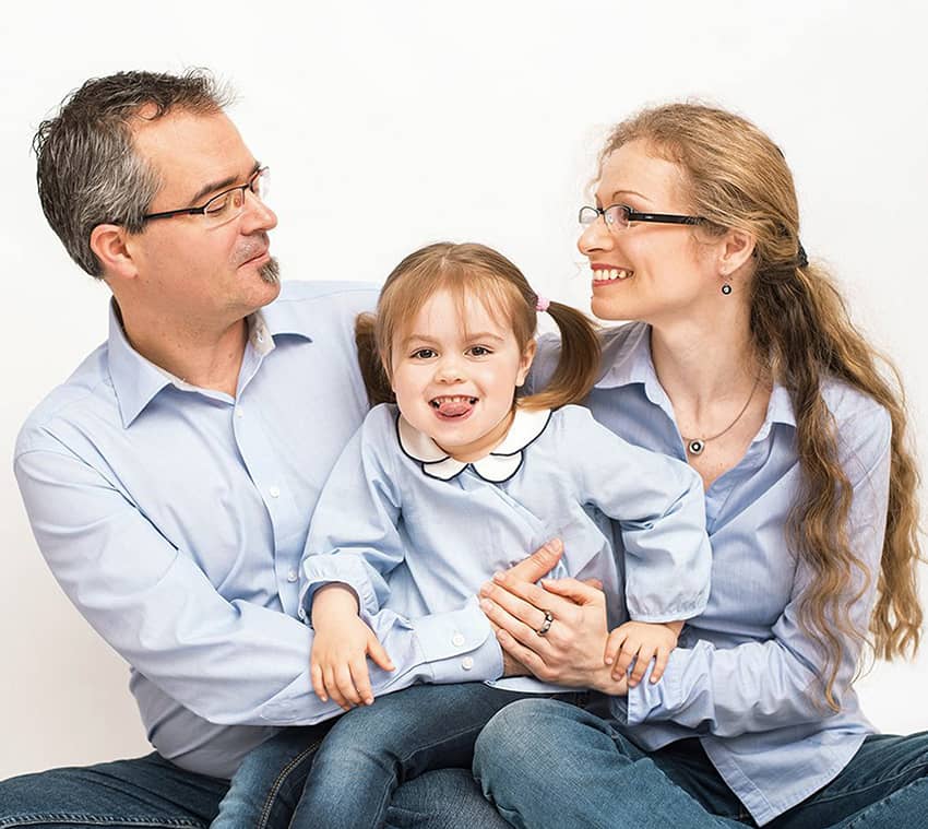 Eine Familie mit einer kleinen Tochter in der Mitte die frech die Zunge raus streckt und die Eltern lachen sich an für ein Familienfoto in Wuppertal
