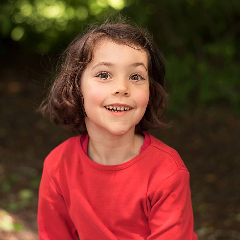 Kinder-Abenteuer-Fotoshooting Wuppertal Fröhliches Mädchen im roten Pullover beim Kinderabenteuer-Fotoshooting im Wald in Wuppertal