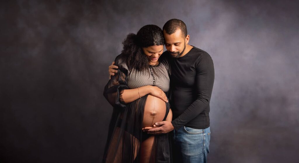 Ein Paar Arm in Arm auf den Bauch der Schwangeren nach unten schauend beim Fotoshooting