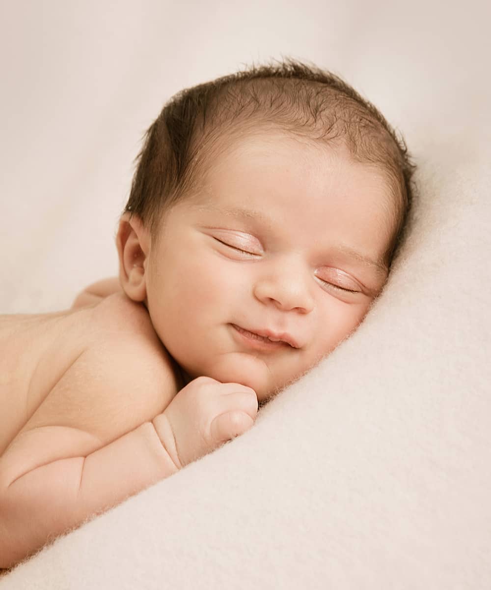 fotoshooting-im-studio-baby-wuppertal seelig lächelndes baby bei einem Newbornshooting in Wuppertal Portraitbild