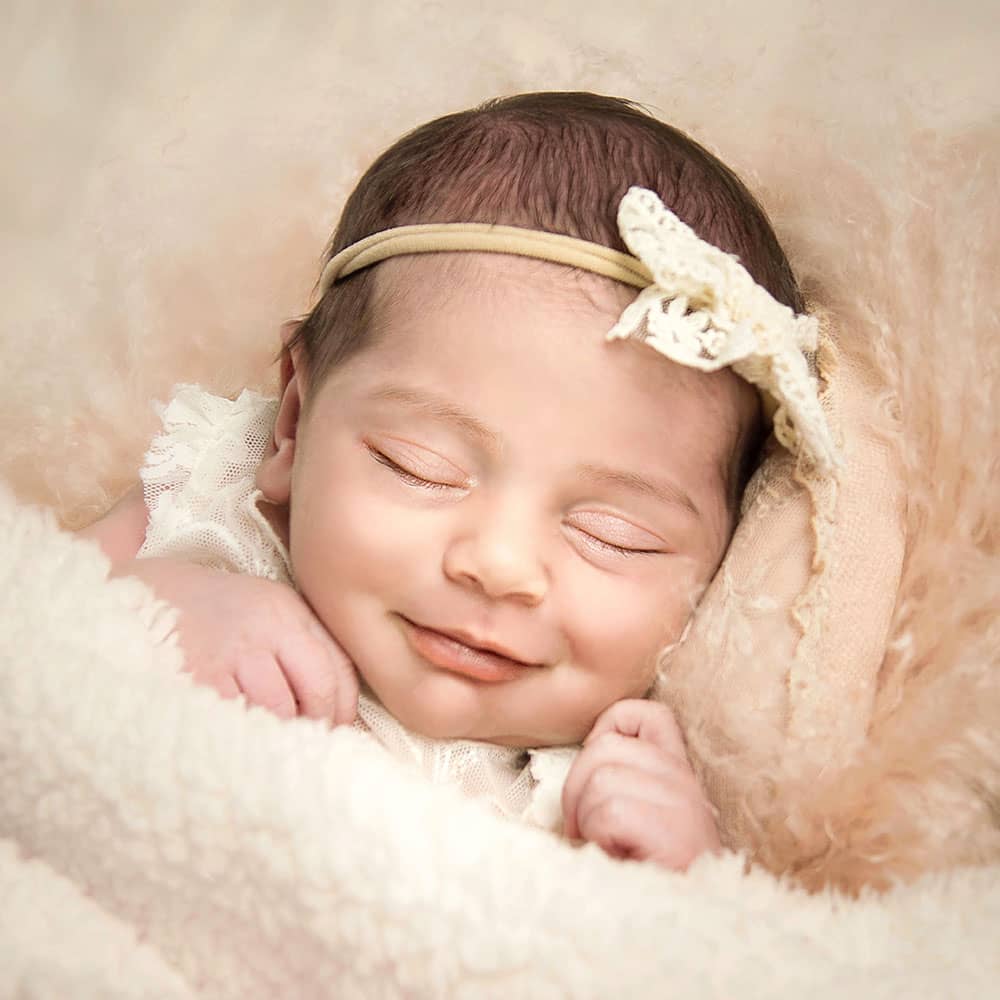 glückliches-neugeborenes-lächelnd-im-fotostudio-wuppertal ein neugeborenes baby liegt glücklich lächelnd mit geschlossenen Augen in einem apricot-farbendem fell beim Fotoshooting im Fotostudio Wuppertal