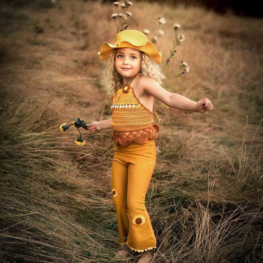 Freies und lebendiges Familien-Fotoshooting in der Natur: Ein kleines Kind hält tanzend Sonnenblumen in der Hand während eines Abenteuer-Shoots in NRW