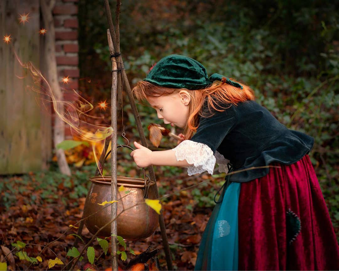 Ein kleines Mädchen mit grünem Kopftuch beugt sich über einen Hexenkessel im Wald und probiert den Zaubertrank beim Kinderfotograf Wuppertal