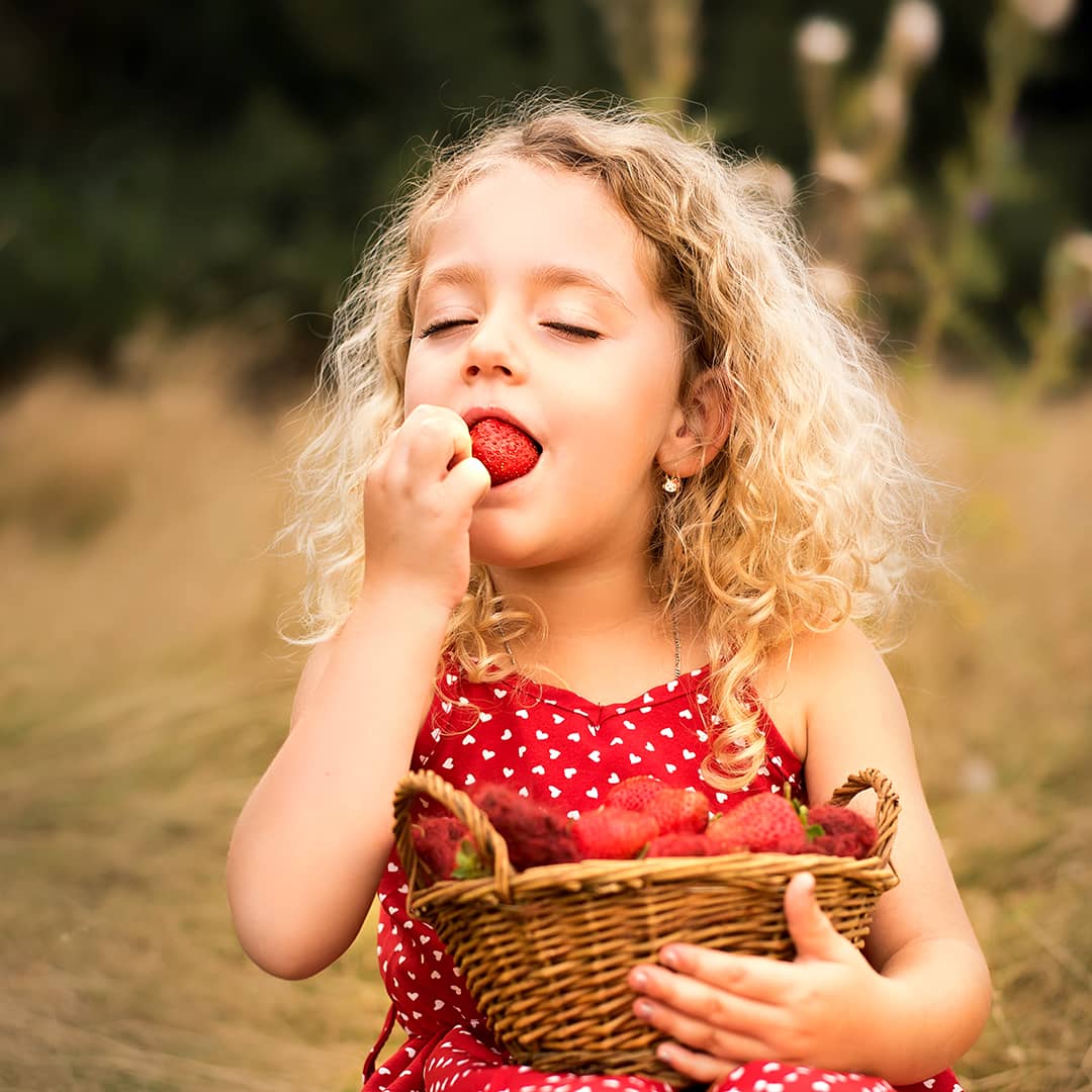 kleines blondes Mädchen beißt sehr genussvoll in eine Erdbeere beim lebendigen Kinder-Fotoshooting in Wuppertal