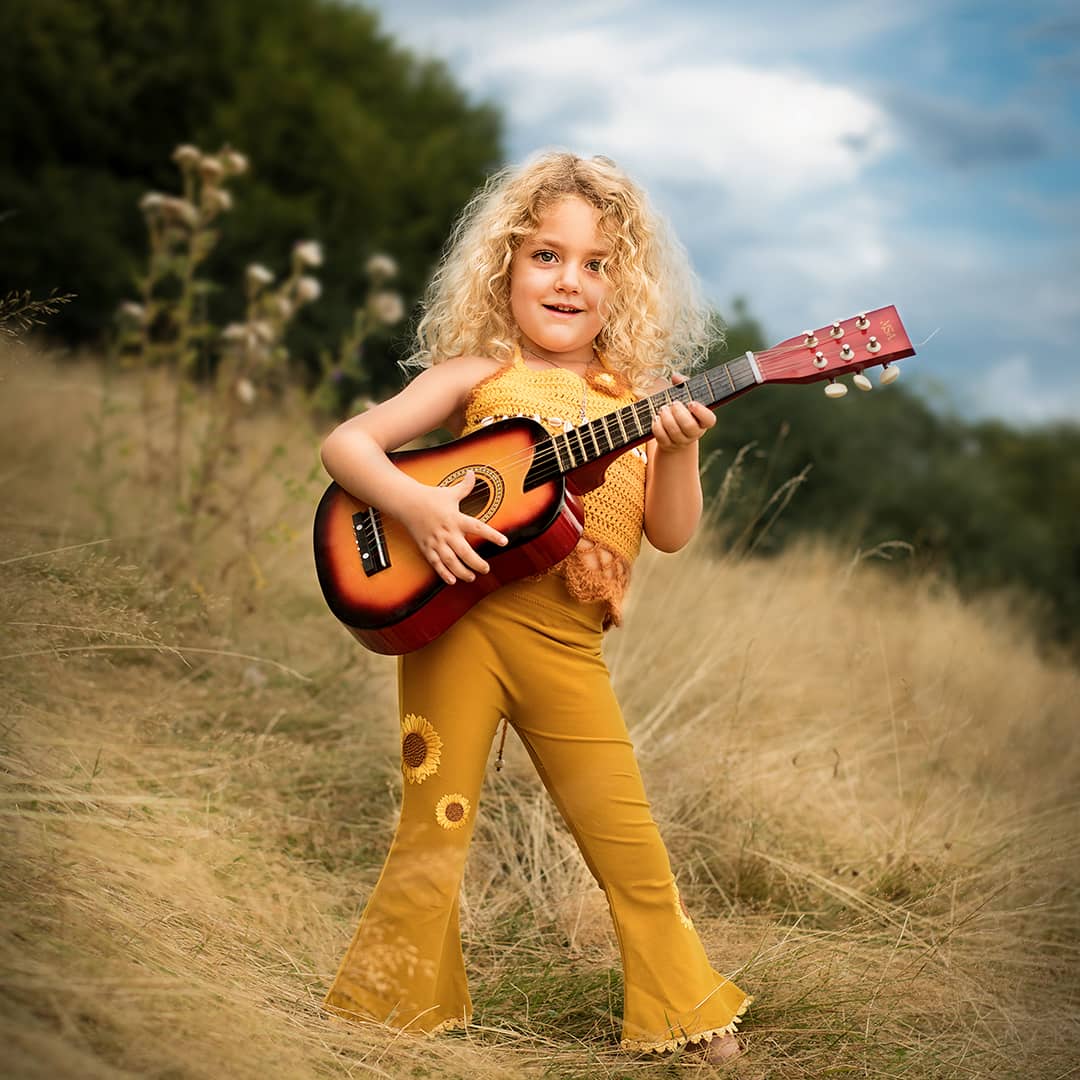 Ein kleiner, ungezähmter Rockstar mit einer Gitarre in der Hand läuft barfuß durch die Natur bei einem ungestellten Kinder-Fotoshooting in Wuppertal