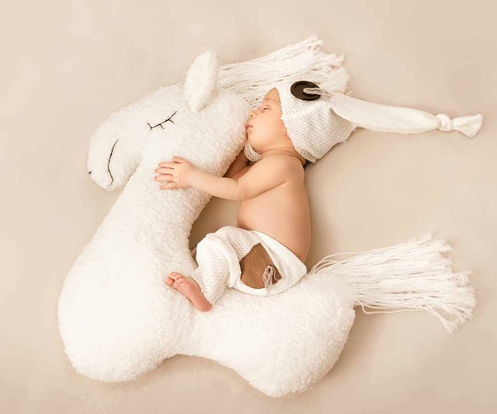 neugeborenes-auf-seepferdchen-fotoshooting-wuppertal baby sitzt auf einem Seepferdchen mit fliegender Zipfelmütze und fliegender Mähne in beige-weiß-Tönen bei der Neugeborenenfotografie im Fotostudio Wuppertal