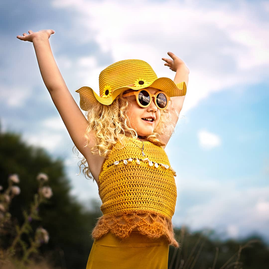 Lebendige Kinderfotografie in Wuppertal: Glückliches Mädchen mit Sonnenbrille und gelbem Hut zeigt sein wildes Herz beim freien Outdoor-Shooting